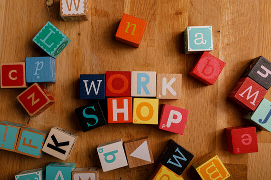 Top-down shot of wooden blocks spelling out the word 'WORKSHOP' surrounded by other alphabet blocks on a wooden surface.