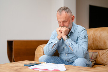 Fototapeta premium Man sitting on couch with documents looking worried in modern living room