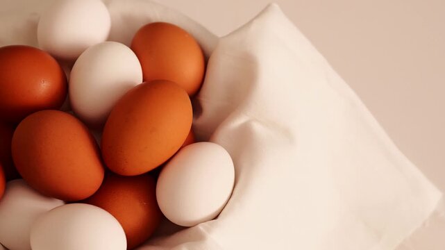 Fresh brown and white eggs sit nestled in a light fabric on a clean white background, ready for a healthy meal