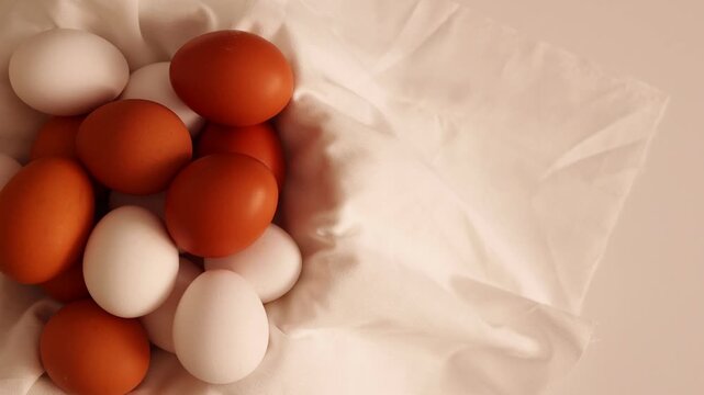 A mix of white and brown eggs rests in a light brown fabric on a white surface, prepared for cooking or baking.