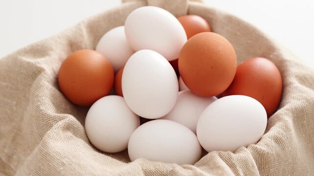 Many fresh brown and white chicken eggs carefully placed on a textured fabric lining a basket for collection