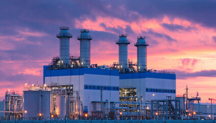 Obraz premium Industrial power plant with three large cooling towers against a vibrant sunset sky.