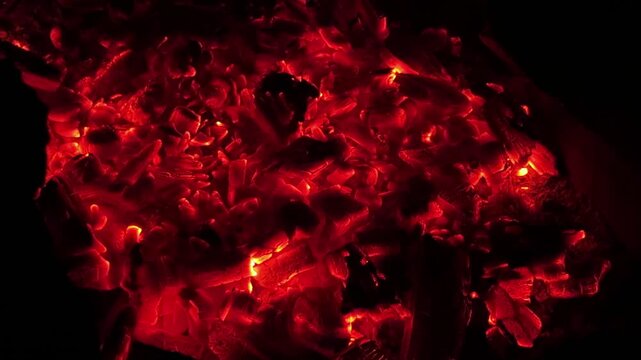 Close up of glowing charcoal embers burning with red and orange tones at night. Soft heat and shimmering texture create magical atmosphere. Warm abstract scene symbolizing warmth and quiet at nature