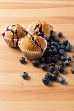 Three Homemade Blueberry Muffins with Scattered Fresh Blueberries on Wooden Table, Vertical 