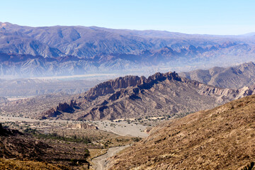 Rugged mountains stretch across a vast arid valley in Bolivia. A dry riverbed winds through the parched landscape on a sunny day