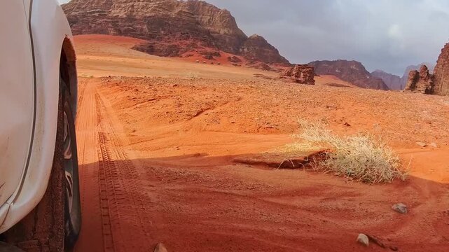 Close up 4wd vehicle driving across Wadi rum red sand track with desert mountains off road adventure travel. SUV driving through gravel dirt road hilly terrain rugged mars alike deserted landscape