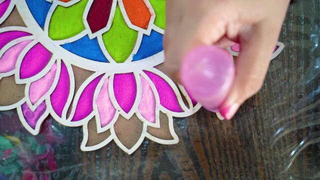 Top down flatlay of powder being poured using a plastic bottle with nozzle into template stencil with vibrant floral pattern on floor decoration for indian hindu festival like diwali holi