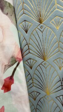 Textured decorative pillows and patterned fabrics closeup featuring floral prints, raised tufted motifs, gold fan geometric print, Video taken on mobile device.