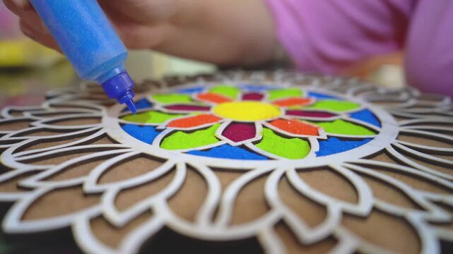 macro close up shot of coloured powder being poured from a plastic bottle into a rangoli stencil template with vibrant floral pattern on the floor showing the traditional decoration of hindu festivals