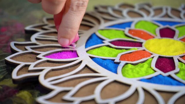 Slow motion macro close up shot of coloured powder being poured by hand into a rangoli stencil template with vibrant floral pattern on the floor showing the traditional decoration of hindu festivals