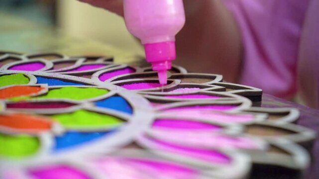 Slow motion macro close up shot of coloured powder being poured from a plastic bottle into a rangoli stencil template with vibrant floral pattern on the floor showing the traditional decoration of