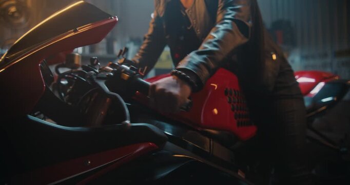 Empowered Woman in Black Leather Outfit Starting Motorcycle in Private Garage. Female Mounts Motorcycle and Revs Engine For Departure. High End Garage Background With Tools and Industrial Siding.