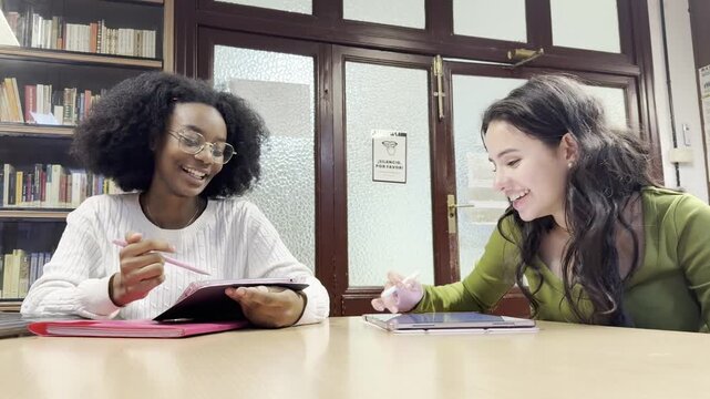 Young multiracial female students happily collaborating on a project with tablets in a library