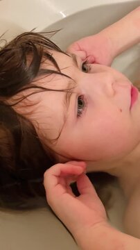Close-up little girl bathing in a bathtub. Water and foam are visible as baby washes herself during a daily routine. Healthy childhood habits and self care development in domestic bathroom setting.