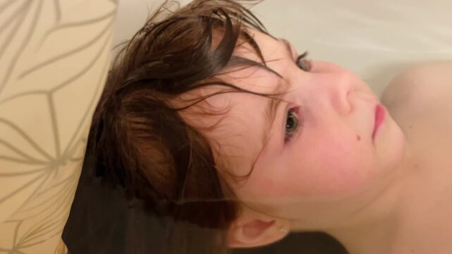 Close-up little girl bathing in a bathtub. Water and foam are visible as baby washes herself during a daily routine. Healthy childhood habits and self care development in domestic bathroom setting.