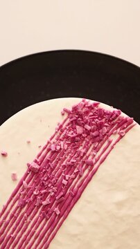 Delicious white cake with vibrant pink decoration and sprinkles on a black plate for a modern dessert