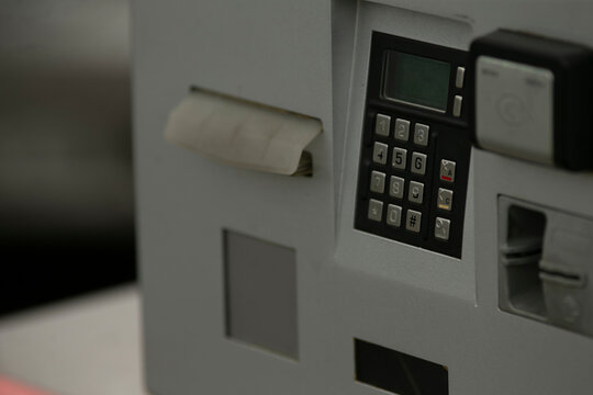Closeup payment terminal urban parking kiosk, metal keypad and card slot with numeric display, contactless logo, scuffed edges, ambient street light,