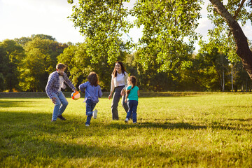 Active children and their parents playing football in park, moving and laughing, spending free time...