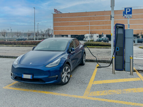 Cuneo, Italy - March 6, 2026: Tesla Model Y electric car connected to an Enel X charging station in a shopping center parking lot