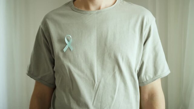 A young man with a blue satin ribbon on his tshirt stands with arms crossed. November is Prostate Cancer Awareness Month for diagnosis and support.