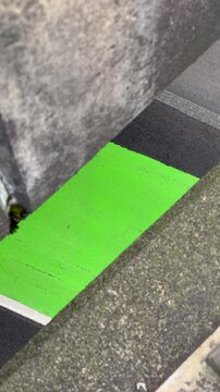 Vertical format of a gap in an overpass, and a peek of  traffic can be seen below. A patch of concrete painted green symbolizes conflict lanes where bikes and vehicles merge into the same lane.