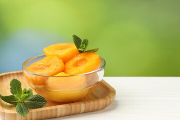 Pickled peaches and mint leaves in bowl on white wooden table, closeup. Space for text © New Africa
