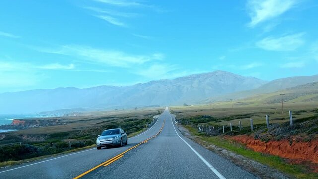 Car driving on Pacific Coast Highway along the ocean. Silver sedan on coastal road with mountains and Pacific sea view in California.