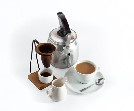 Traditional Brazilian coffee set with aluminum kettle, cloth filter, and a cup of coffee with milk on white background.