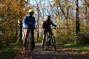Naklejka premium Smiling couple cycling together on autumn forest path. Active lifestyle and outdoor recreation concept.