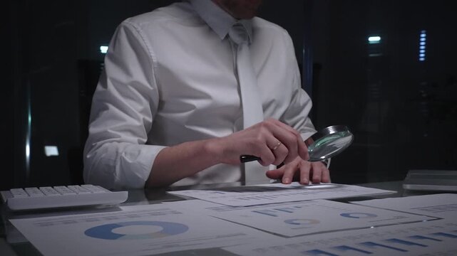 Businessman holding a magnifying glass and checking financial data, reviewing corporate audit reports, and analyzing various charts. Audit and taxes in business