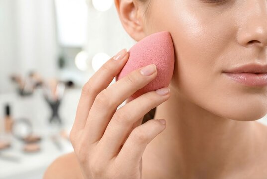 Close up of young woman applying liquid foundation on her face with a pink makeup sponge