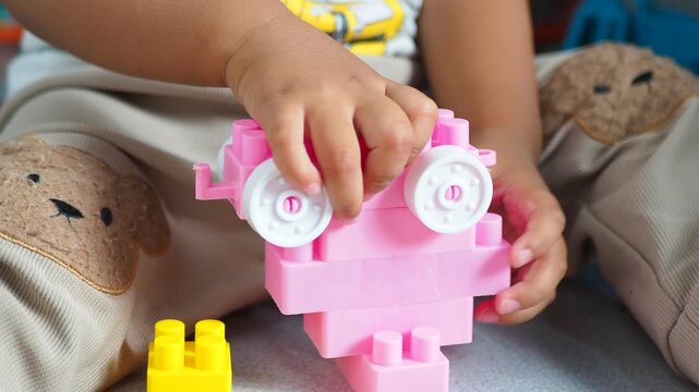 Close-up of a toddler's hands playing with colorful plastic construction building blocks, fostering creativity and motor skills.