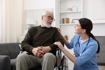 Obraz premium Care worker supporting senior man in wheelchair indoors