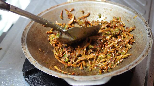 Close-up of fried anchovies with chilies and onions being stirred in a wok