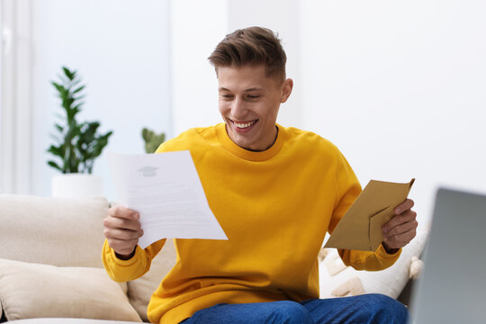 Happy man with acceptance letter from university on sofa at home
