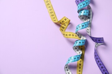 Different measuring tapes on lilac background, flat lay. Space for text