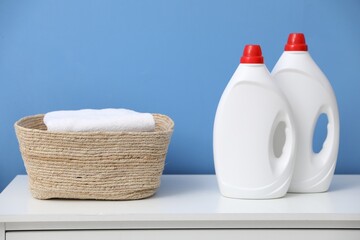 Clean towels in laundry basket and bottles of detergents on white cabinet near blue wall indoors