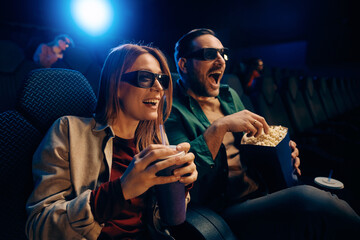 Excited couple enjoying in 3D film screening at cinema.