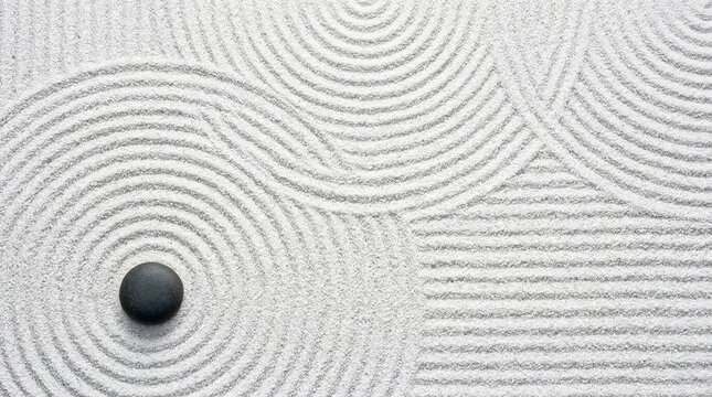 top view of single black zen stone on white sand with raked circular patterns for meditation and mindfulness background concept