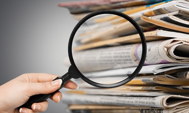 Hand holds Magnifying glasson newspapper background
