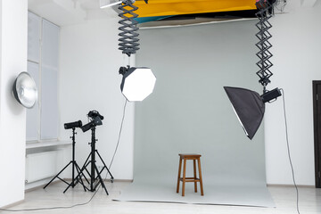 Professional lighting equipment hanging from ceiling and chair in photo studio