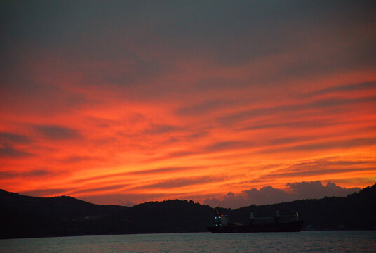 Colorful blue hour sunset over the Adriatic Sea with the dark silhouette of Ugljan Island on the horizon. Dramatic clouds painted with orange, pink and purple tones reflect on the calm water.
