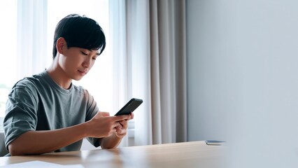 テーブルでスマートフォンを操作する若い男性