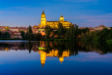 Fototapeta premium Salamanca, Castilla y Leon, Spain: Twilight view of the Cathedral of Salamanca illuminated and reflected int he waters of river Tormes; the Old Cathedral, Cathedral of Santa Maria