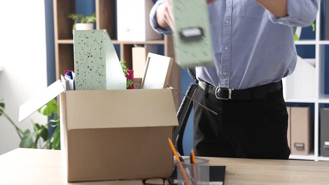 Dismissal. Man packing his personal belongings into cardboard box at wooden table in office, closeup