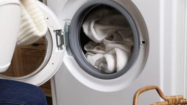 Woman adding detergent into washing machine with towels at home, closeup