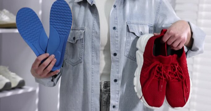 Woman holding orthopedic insoles and shoes indoors, closeup