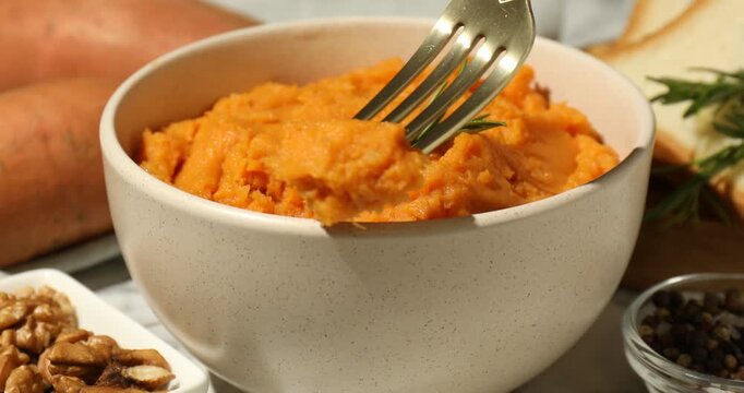 Eating tasty mashed sweet potato with rosemary at table, closeup