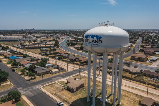 Aerial Drone View of Tall White Water Tower Surrounded By Buildings and Streets With Blue Sky in Downtown Midland, Texas