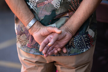 Man's hands clasped behind back, unposed movement, natural candid motion, hand skin and nail texture, close-up, at Chatuchak Market.
